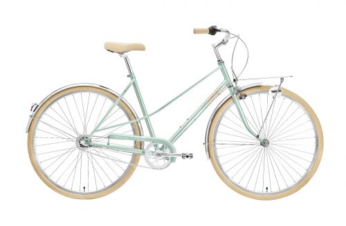 The Creme Caferacer Lady Uno Urban Bike in Florida Green. Road bike 2022 version. Equipped with full chrome mudguards, cream saddle, handles, and tyres. Front headlamp and pannier. Side-on view.